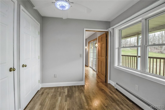 unfurnished bedroom featuring baseboards, ceiling fan, a baseboard heating unit, and wood finished floors
