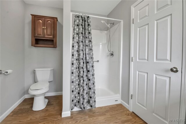 full bath with baseboards, wood finished floors, a shower stall, and toilet