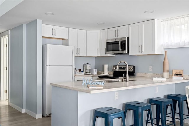6186 Reservoir Rd, Lebanon, NY 13346 - kitchen with stainless steel appliances, a peninsula, white cabinets, light wood-style flooring, and a kitchen breakfast bar