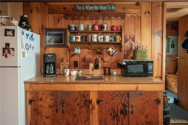 kitchen with black microwave, wooden walls, electric panel, and freestanding refrigerator