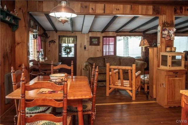 dining space featuring beamed ceiling, wooden walls, and wood finished floors