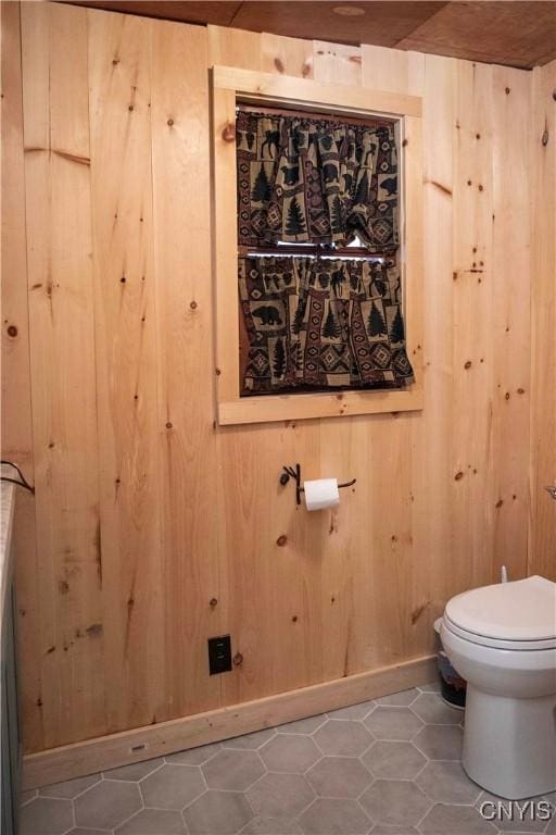bathroom featuring wooden walls, toilet, and baseboards