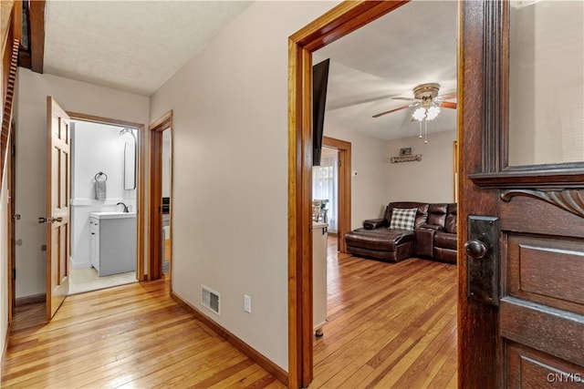 hall with light wood finished floors, a sink, and baseboards