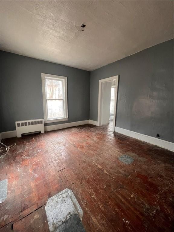 unfurnished room featuring a baseboard radiator, baseboards, a healthy amount of sunlight, and wood-type flooring