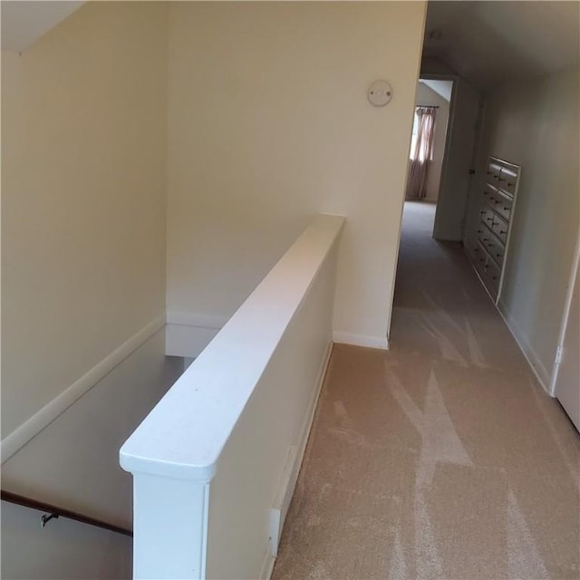 corridor with an upstairs landing, light carpet, and baseboards