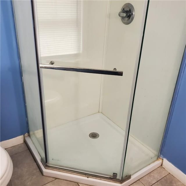 full bathroom featuring a stall shower, baseboards, tile patterned floors, and toilet