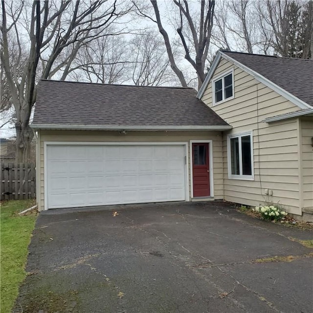 view of front of home featuring roof with shingles, asphalt driveway, and fence