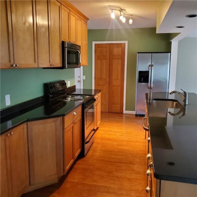 kitchen featuring stainless steel appliances, a sink, dark countertops, and light wood finished floors