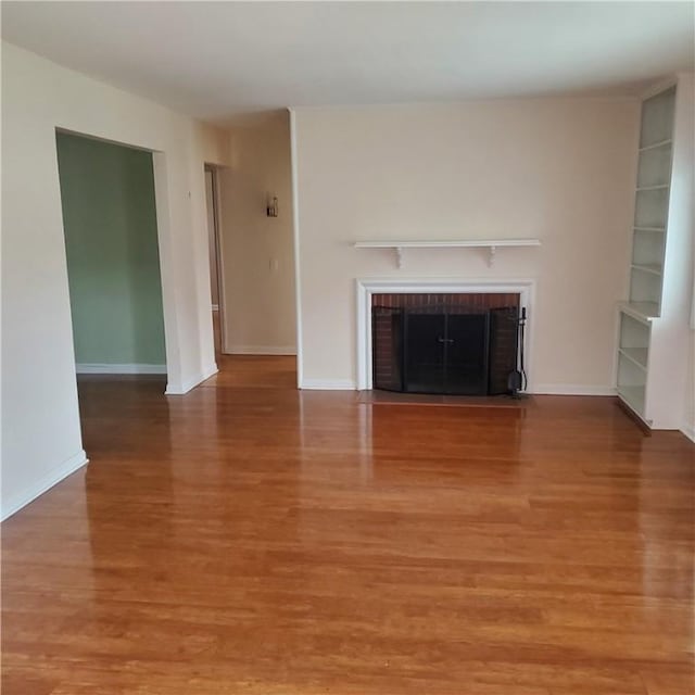 unfurnished living room featuring a brick fireplace, light wood finished floors, and baseboards