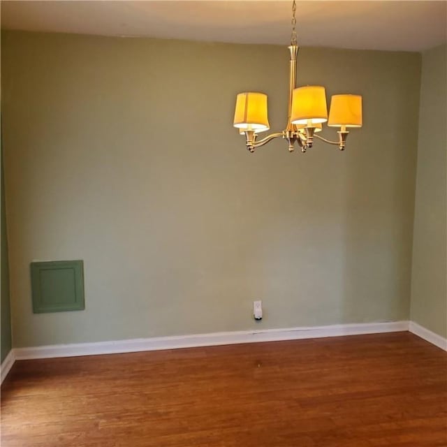 spare room featuring a chandelier, wood finished floors, and baseboards