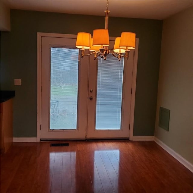 unfurnished dining area featuring wood finished floors, baseboards, french doors, and a chandelier