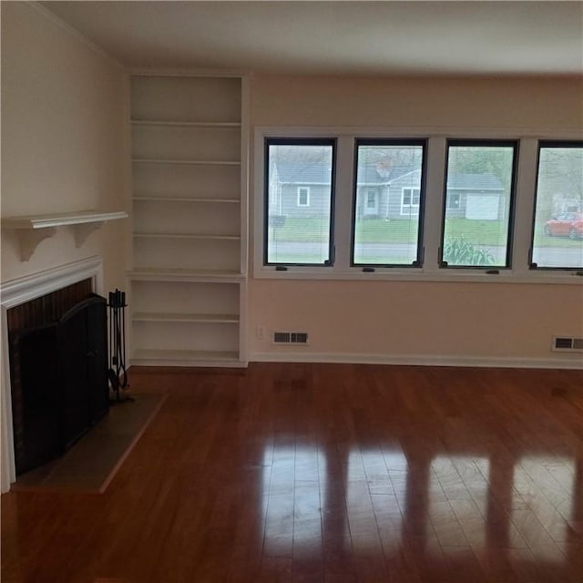 unfurnished living room with hardwood / wood-style flooring, built in features, a fireplace, and baseboards