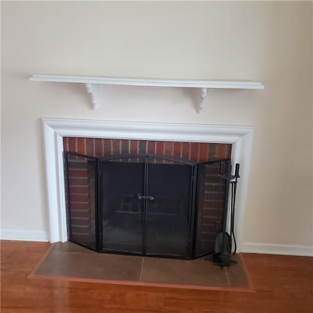detailed view of a brick fireplace, baseboards, and wood finished floors