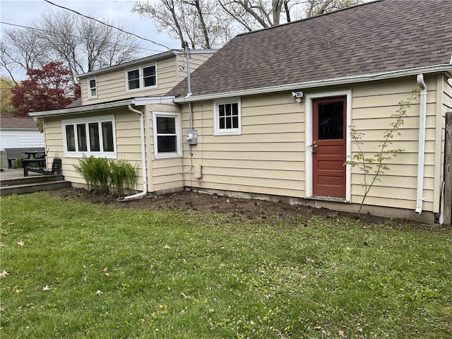 rear view of property featuring a shingled roof and a lawn