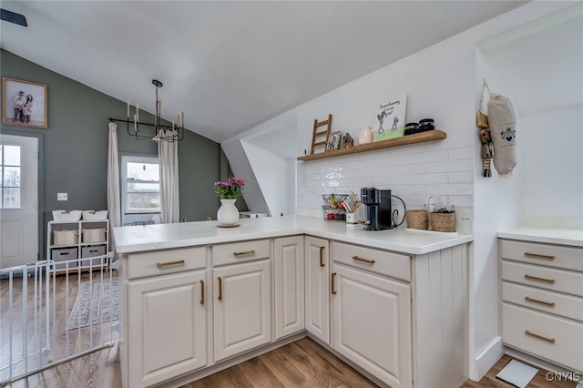 kitchen with light wood-style flooring, a peninsula, light countertops, backsplash, and lofted ceiling