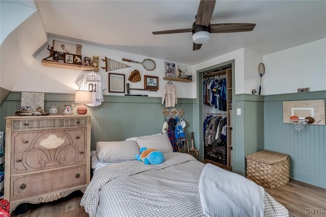bedroom with a wainscoted wall, wood finished floors, a closet, and ceiling fan