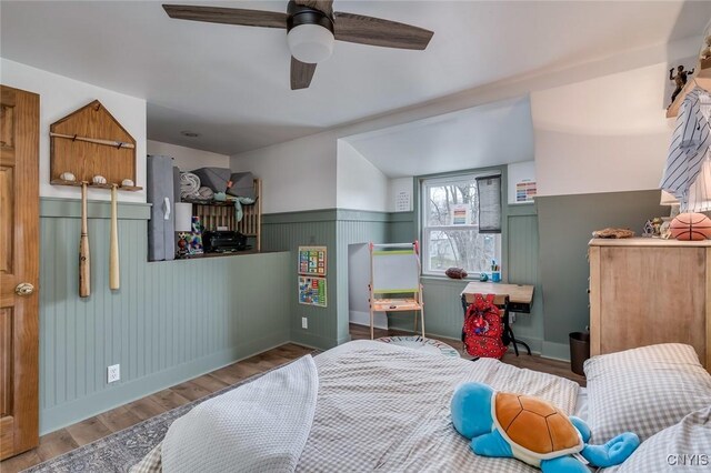 bedroom featuring wood finished floors, a wainscoted wall, baseboards, and a ceiling fan