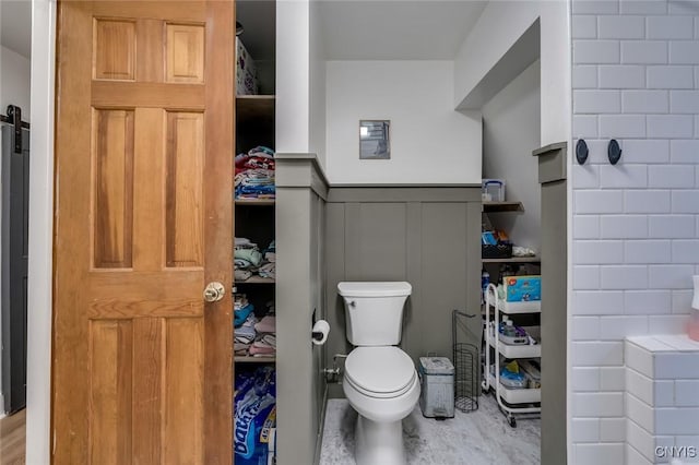 bathroom with toilet, a wainscoted wall, and a decorative wall