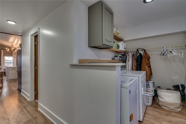 laundry area featuring cabinet space, light wood finished floors, washer and dryer, and a notable chandelier