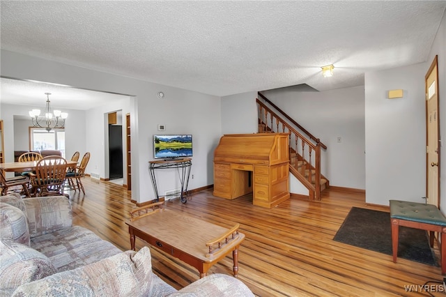 living area featuring stairway, baseboards, light wood-style flooring, a textured ceiling, and a notable chandelier