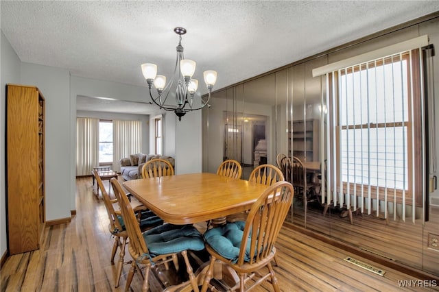 dining room featuring wood finished floors, a textured ceiling, a notable chandelier, and visible vents