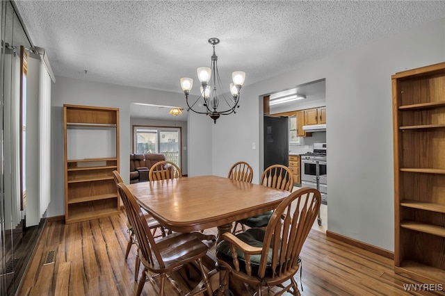 dining area with a textured ceiling, dark wood-style flooring, baseboards, visible vents, and an inviting chandelier