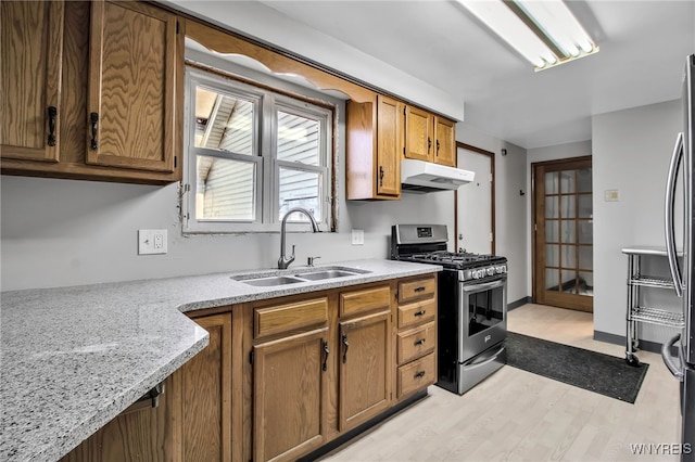 kitchen featuring a sink, brown cabinetry, light wood-style floors, stainless steel range with gas stovetop, and under cabinet range hood