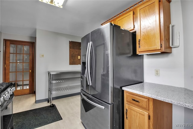 kitchen with stainless steel fridge with ice dispenser, light stone counters, black gas range, and light wood-style flooring