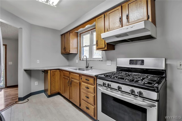 kitchen featuring brown cabinetry, under cabinet range hood, a sink, and gas range