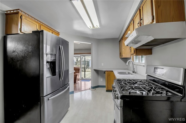kitchen with under cabinet range hood, stainless steel appliances, light countertops, a sink, and light wood-style flooring