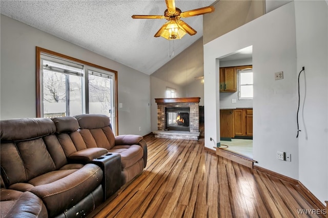 living area with a ceiling fan, light wood-style floors, baseboards, lofted ceiling, and a brick fireplace