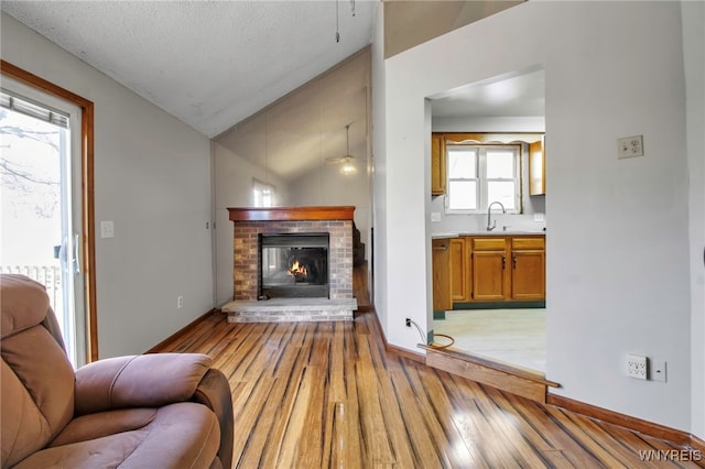 living area featuring baseboards, vaulted ceiling, light wood-type flooring, and a fireplace