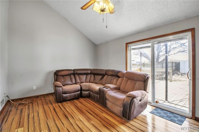 living room featuring light wood-style flooring, a textured ceiling, vaulted ceiling, baseboards, and a ceiling fan