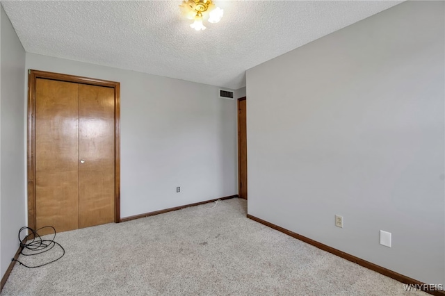 unfurnished bedroom featuring a textured ceiling, baseboards, light carpet, and visible vents