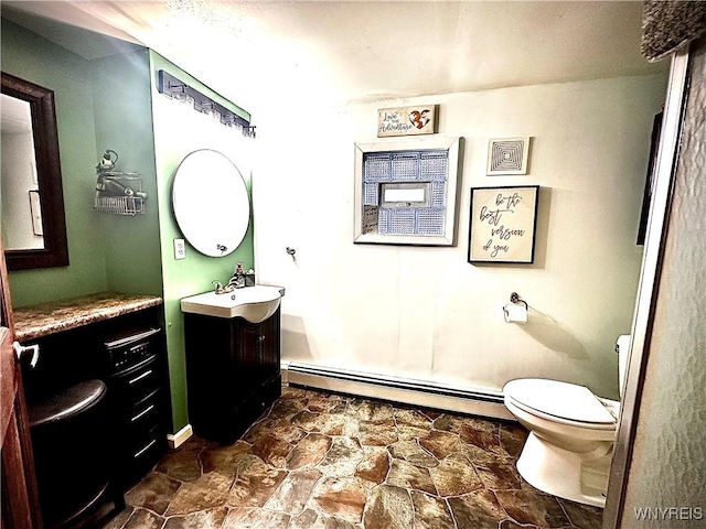 bathroom featuring a baseboard heating unit, toilet, vanity, and stone finish flooring