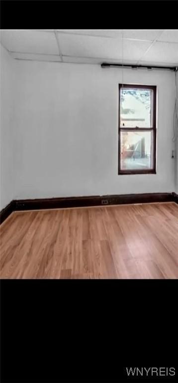 unfurnished room with baseboards, a drop ceiling, and wood finished floors