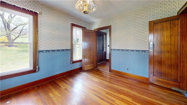 4501 State Route 414, Hector, NY 14818 - empty room featuring wallpapered walls, baseboards, wood finished floors, and a notable chandelier