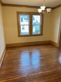 empty room with dark wood-type flooring, crown molding, an inviting chandelier, and baseboards