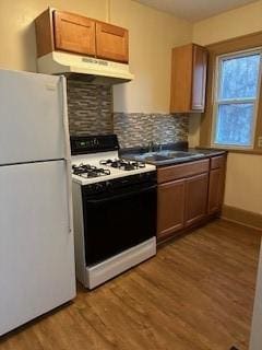 kitchen with tasteful backsplash, white appliances, dark countertops, under cabinet range hood, and light wood-style floors