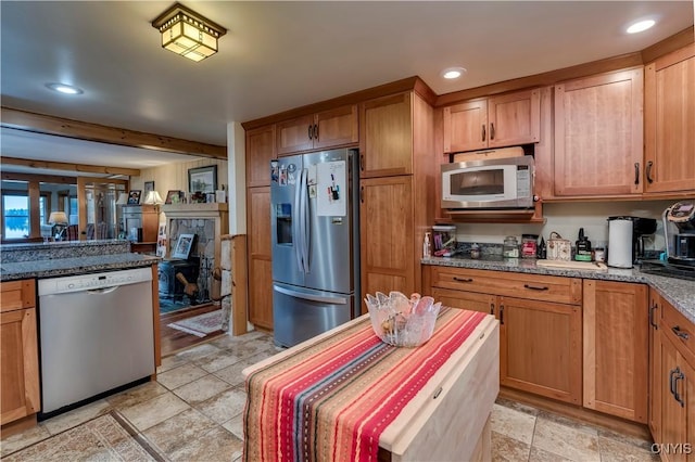 kitchen featuring dark stone counters, brown cabinetry, stainless steel appliances, stone finish floor, and recessed lighting