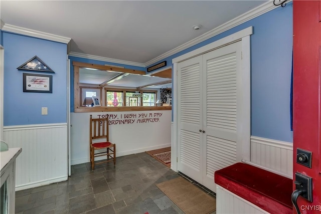 interior space with crown molding, stone finish flooring, and a wainscoted wall