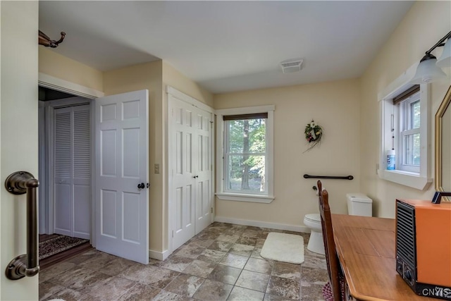 bathroom with toilet, a closet, stone finish flooring, baseboards, and visible vents
