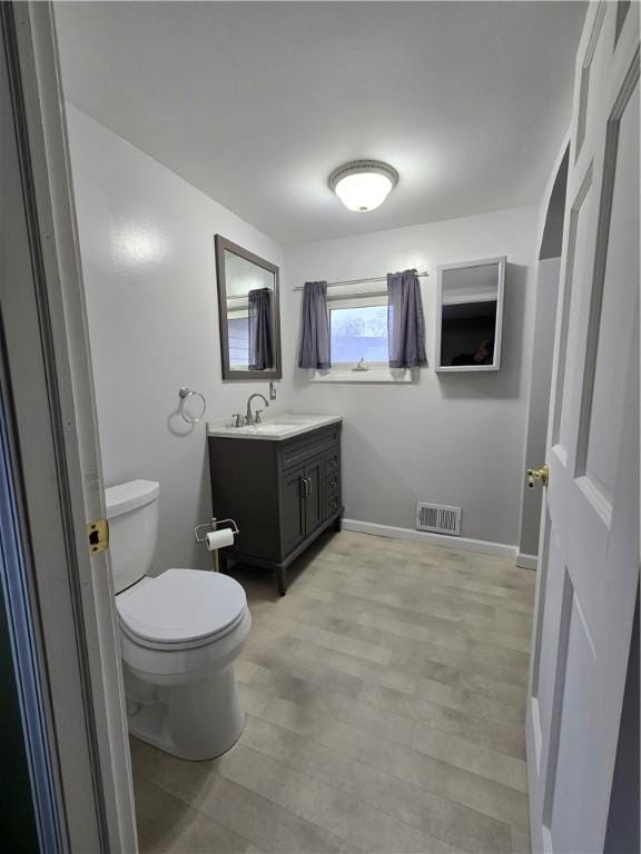 bathroom featuring wood finished floors, visible vents, toilet, vanity, and baseboards