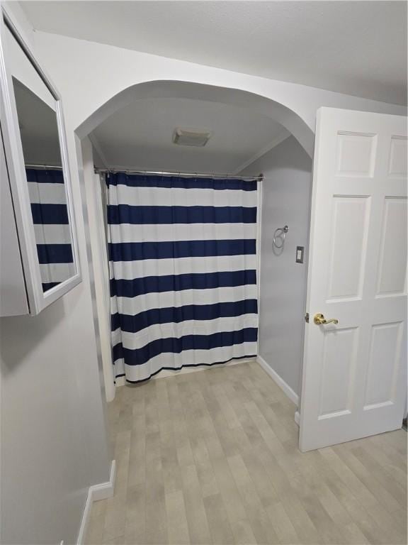 corridor featuring arched walkways, light wood finished floors, and baseboards