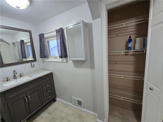 bathroom featuring a walk in closet, baseboards, vanity, and visible vents