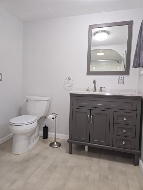 bathroom with wood finished floors, vanity, toilet, and baseboards