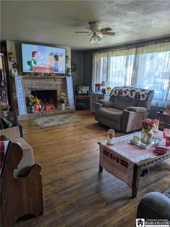 living area featuring a fireplace, wood finished floors, a textured ceiling, and ceiling fan