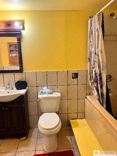 full bath featuring tile patterned floors, toilet, vanity, tile walls, and wainscoting