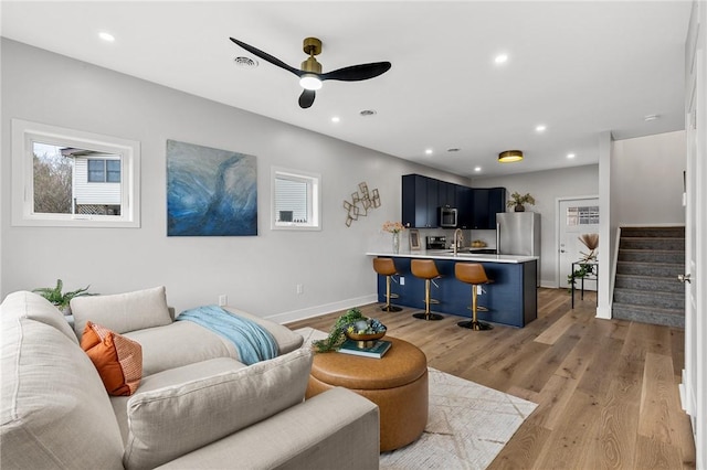 living area with stairway, a ceiling fan, light wood-style flooring, baseboards, and recessed lighting