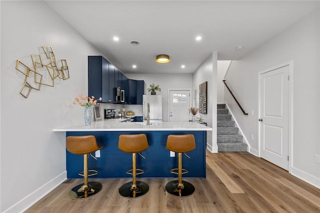 kitchen with blue cabinetry, a peninsula, wood finished floors, and stainless steel appliances